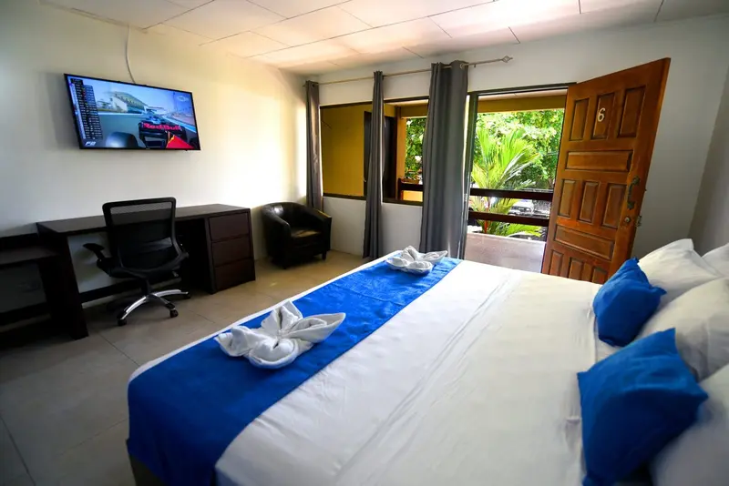 Habitación con cama king de cabecera azul, escritorio con silla de oficina y puerta al jardín