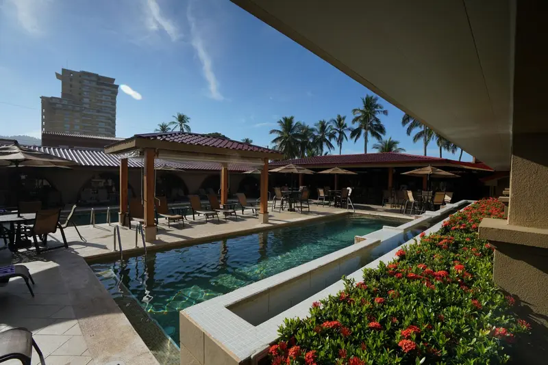 Piscina larga con jardín de flores rojas y palmeras, vista desde el balcón