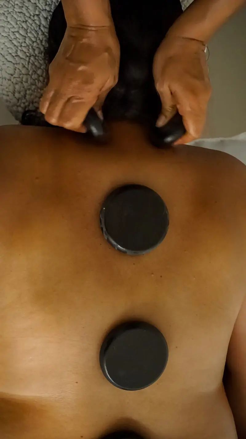 Espalda con piedras negras calientes y manos de la terapeuta