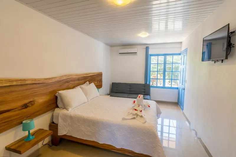 Habitación Clásica con cama de cabecera de madera, televisor y aire acondicionado