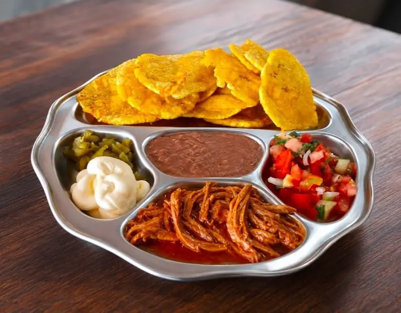 Bandeja de metal con patacones, frijoles, pico de gallo, jalapeños y carne desmenuzada
