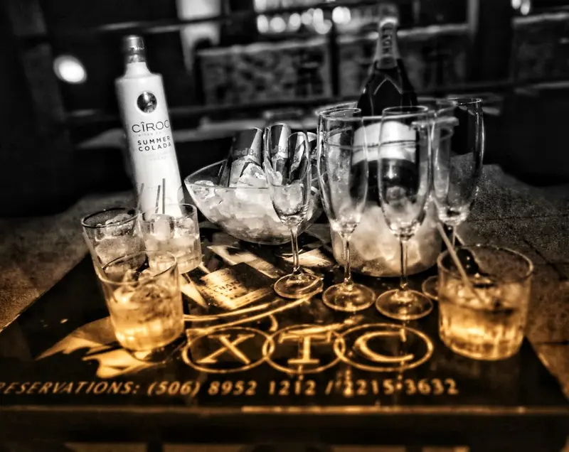 Mesa con botellas, copas y vasos con hielo, en blanco y negro