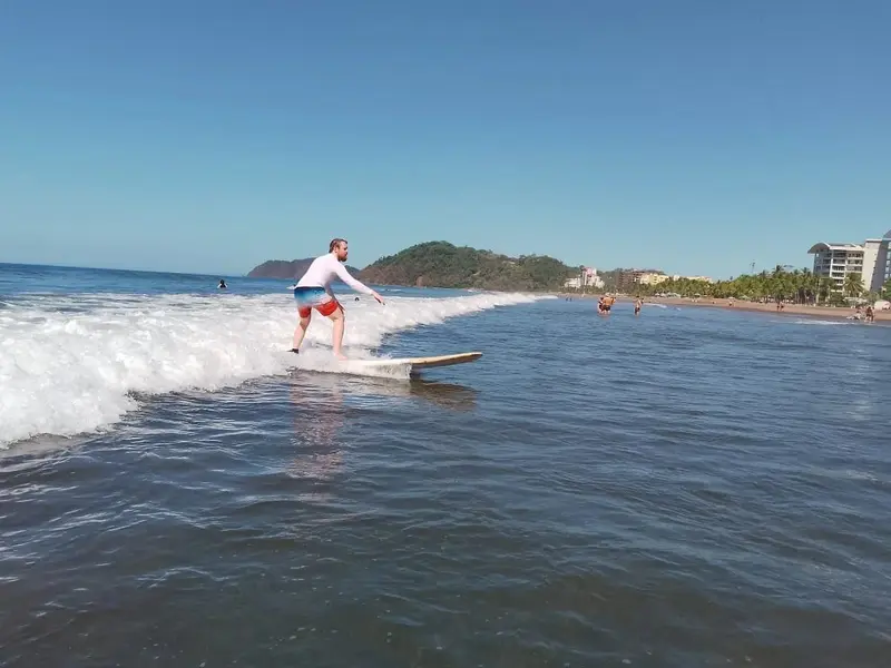 Surfista sobre una ola a lo largo de la playa, con colinas y edificios de la costa al fondo