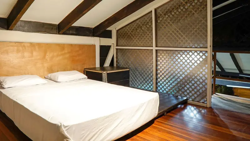 Habitación tipo loft con cama doble, vigas de madera y paneles de celosía