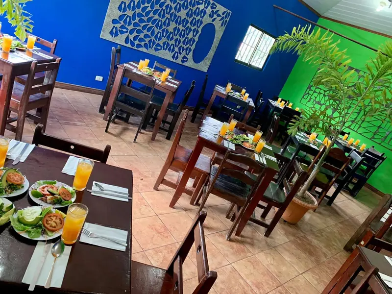 Salón con mesas de madera, paredes azul y verde y vasos de fresco servidos en las mesas