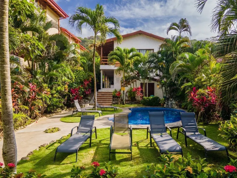Fachada del aparthotel entre jardines, con piscina y camastros