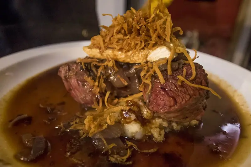 Filete de carne con cebolla crujiente y salsa oscura sobre puré