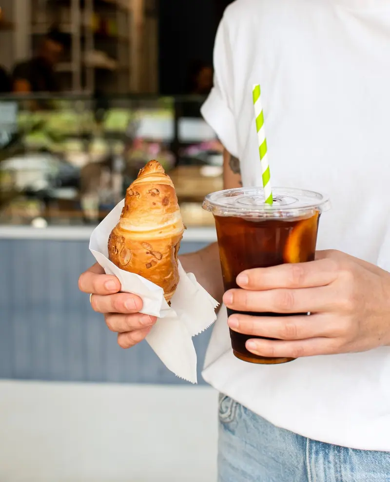 Croissant en papel y un vaso de café frío con pajilla verde, para llevar