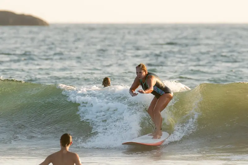 Surfer riding a wave in warm evening light as another person watches from the water