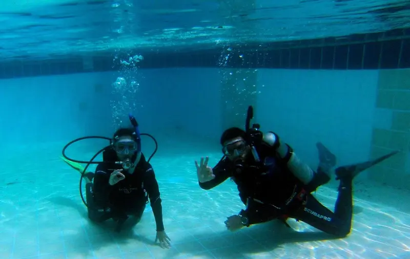 Dos buzos bajo el agua en una piscina haciendo la seña de OK durante un curso Discover