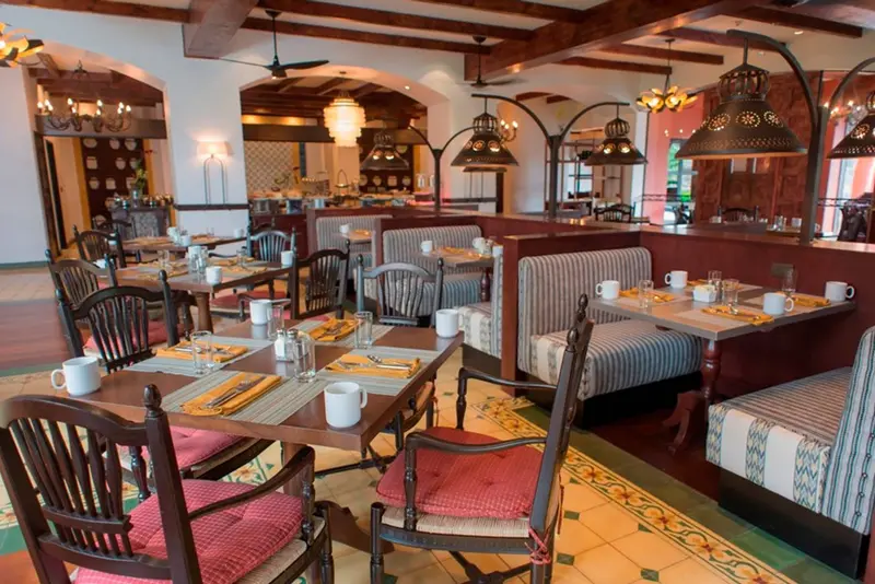 Mesas con sillas de madera y cojines rojos y bancos a rayas en un comedor con arcos