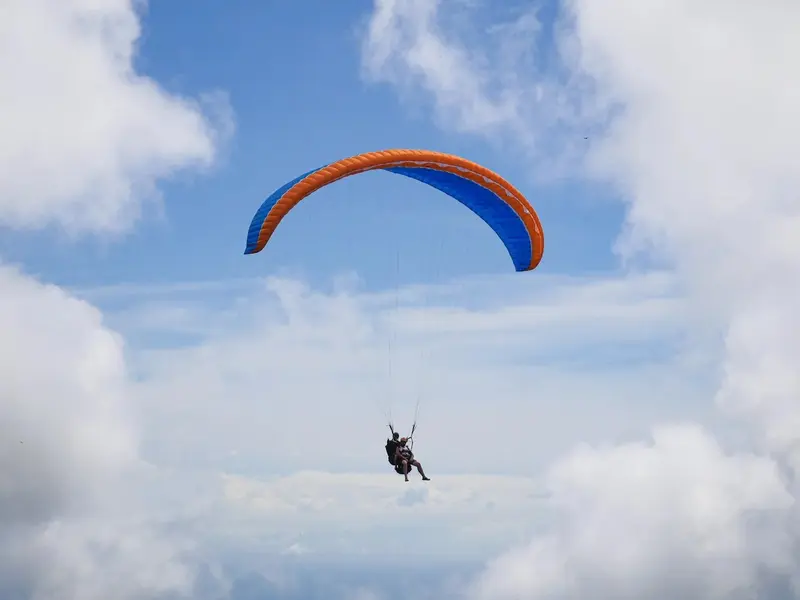 Parapente naranja y azul volando entre nubes, visto de lejos