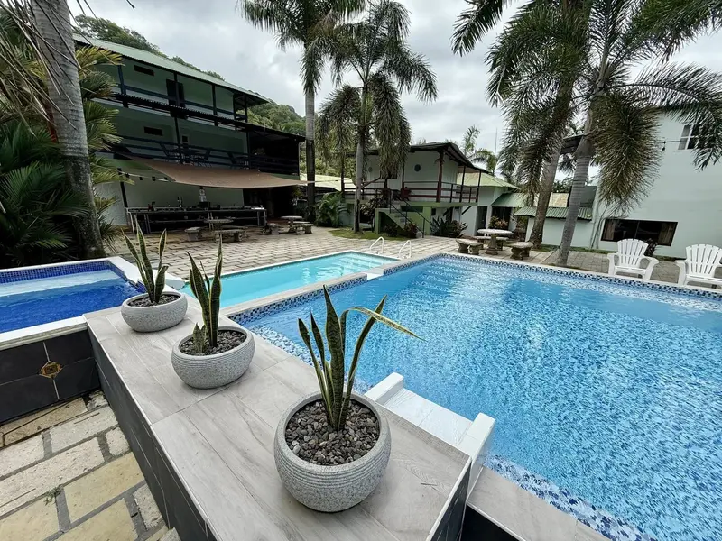Piscina con macetas de agaves en el borde y los edificios del hotel entre palmeras al fondo