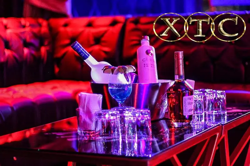 Mesa VIP con una hielera, botellas y vasos sobre un sofá de cuero rojo bajo luces rojas