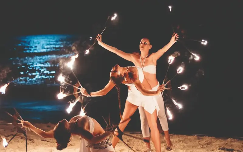Bailarines de fuego con antorchas encendidas en la playa de noche