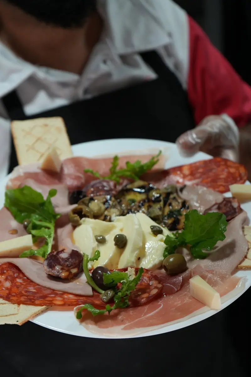 Tabla de antipasto con prosciutto, mortadela, mozzarella y vegetales en un plato blanco