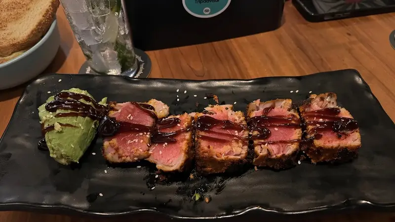 Atún sellado en rebanadas con salsa oscura y puré de aguacate sobre un plato negro