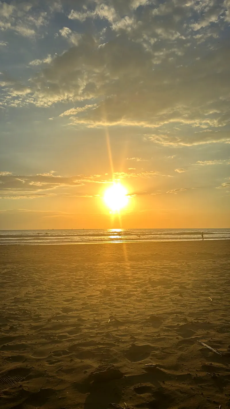 Atardecer real desde Playa Hidalgo en Jacó, con el sol sobre el Pacífico y arena en primer plano