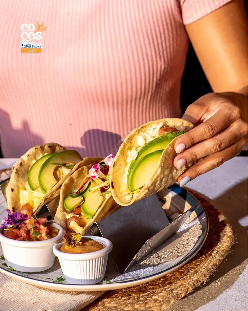 Tacos de maíz con aguacate y camarones sobre un plato, con salsas al lado