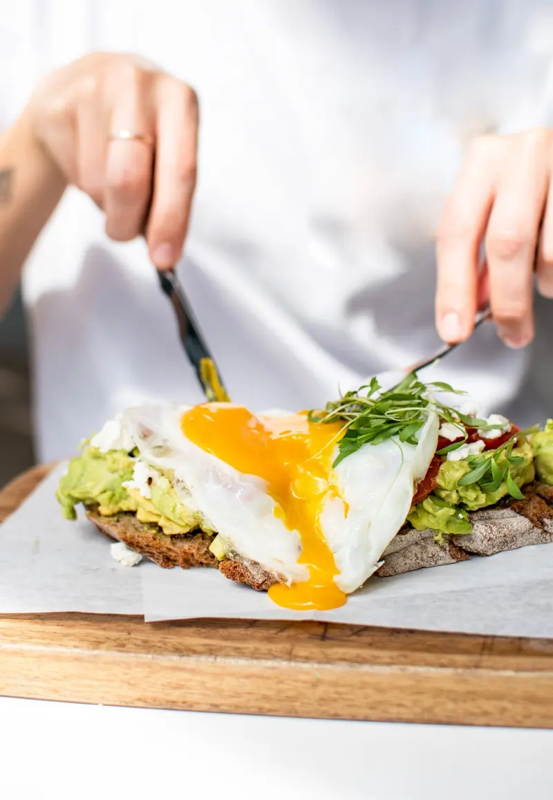 Tostada de aguacate con huevo de yema líquida y microhierbas sobre una tabla