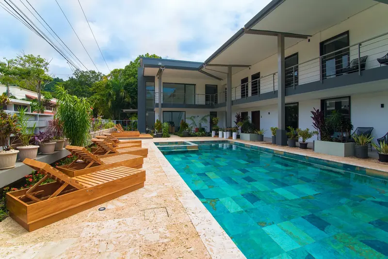 Piscina turquesa con reposeras de madera y los edificios de habitaciones al fondo