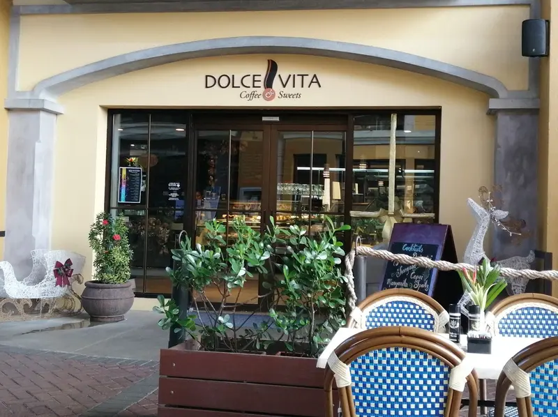 Fachada de Dolce Vita con su rótulo, macetas y mesas en la terraza