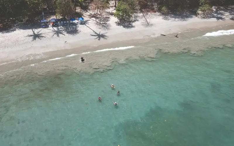 Vista aérea de una playa de arena blanca con gente nadando en agua turquesa