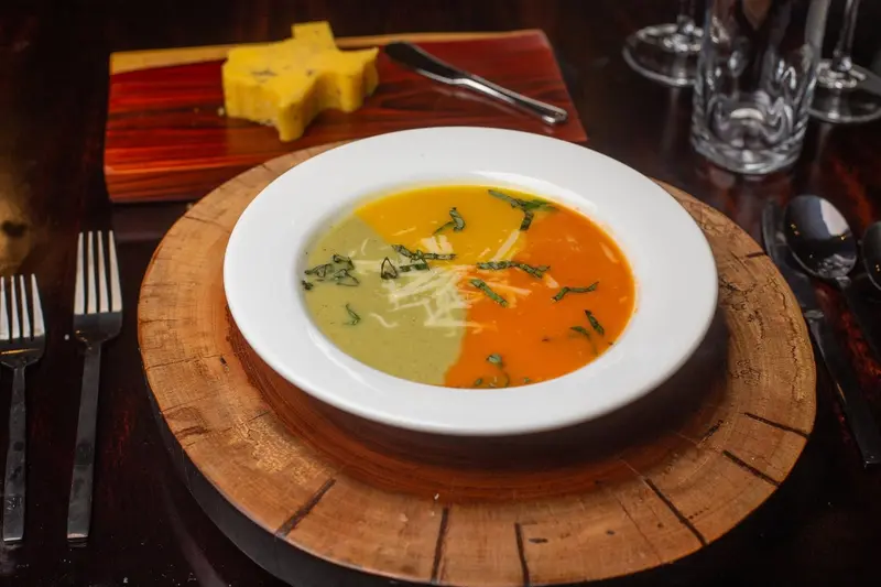 Sopa de dos colores, verde y naranja, servida en un plato hondo sobre una tabla redonda