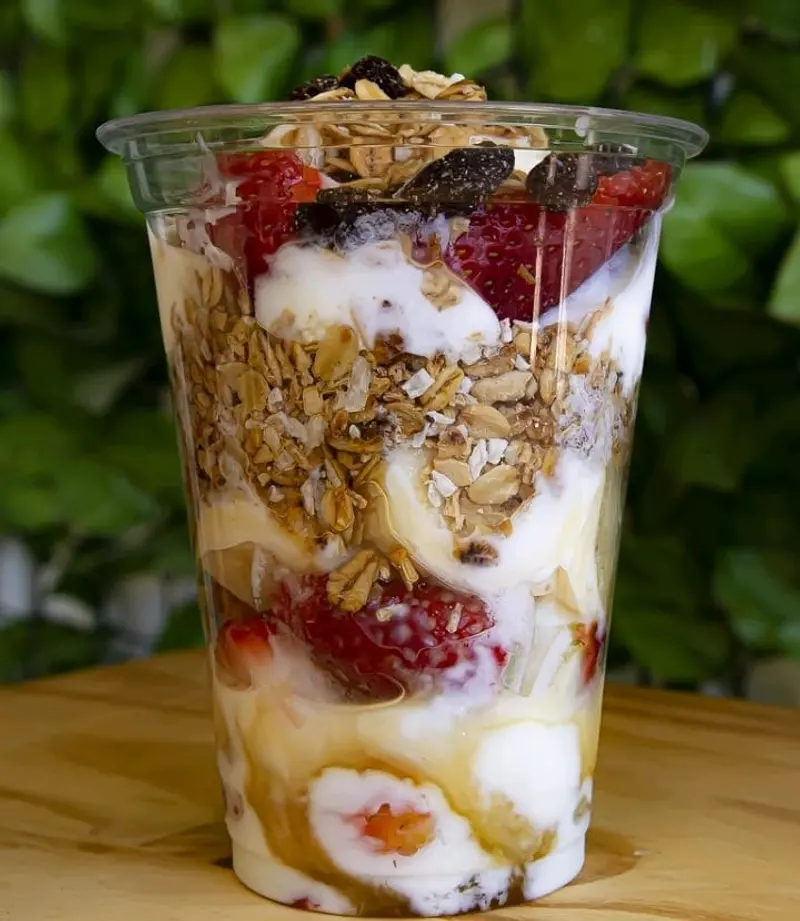 Parfait en un vaso alto con yogurt, granola, fresas y banano
