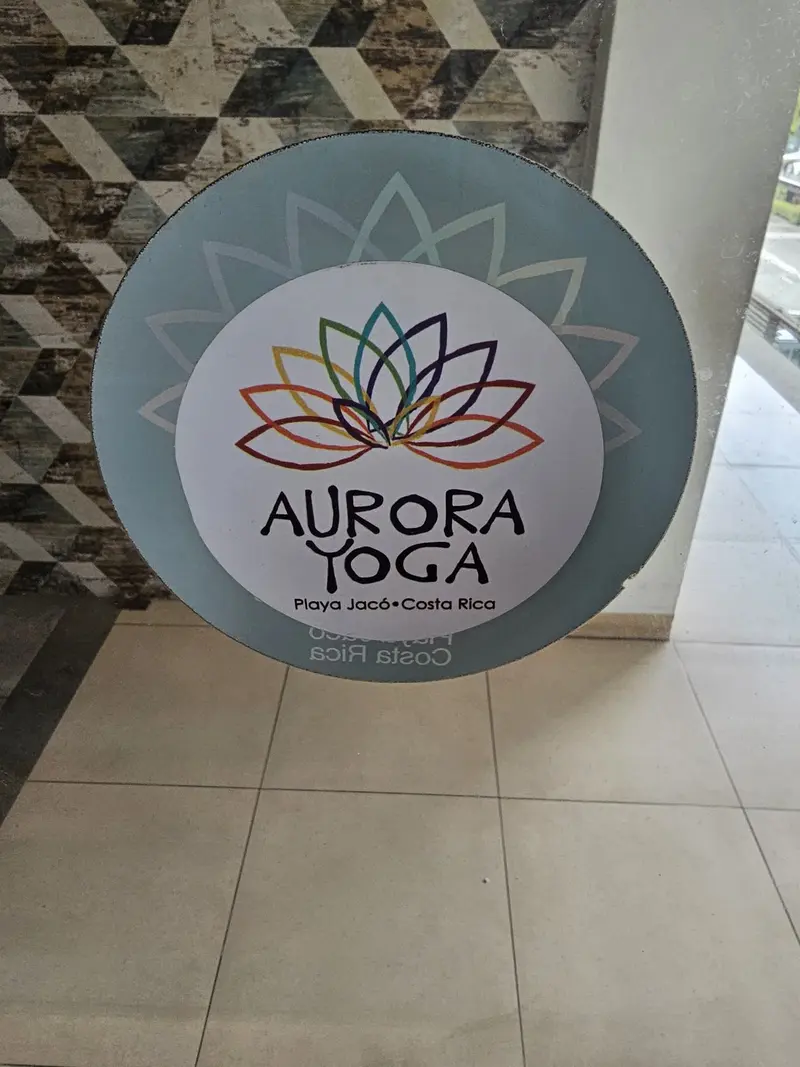 Letrero circular de Aurora Yoga con una flor de loto de colores, sobre un piso de cerámica