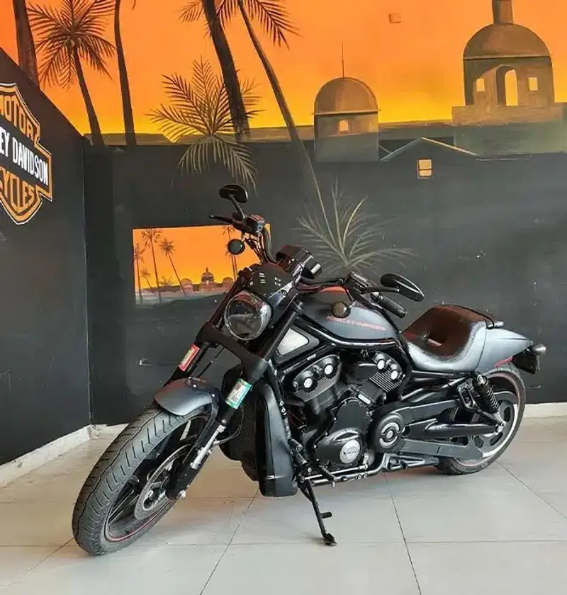 Harley-Davidson Night Rod negra frente a un mural de atardecer