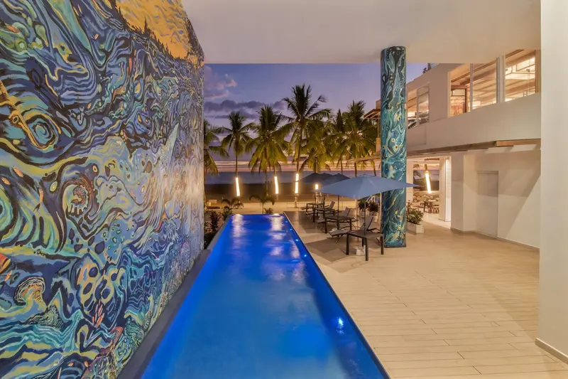 Piscina larga iluminada al anochecer junto a un mural de colores en la pared