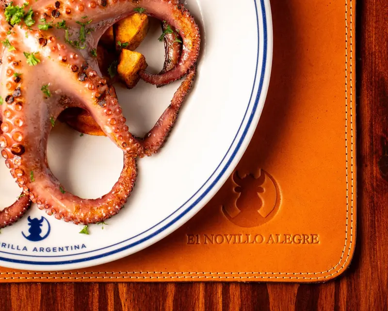 Pulpo a la parrilla con papas en un plato blanco con el logo del restaurante