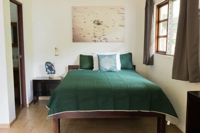 Habitación con cama de matrimonio de cubrecama verde, puerta al baño y ventana