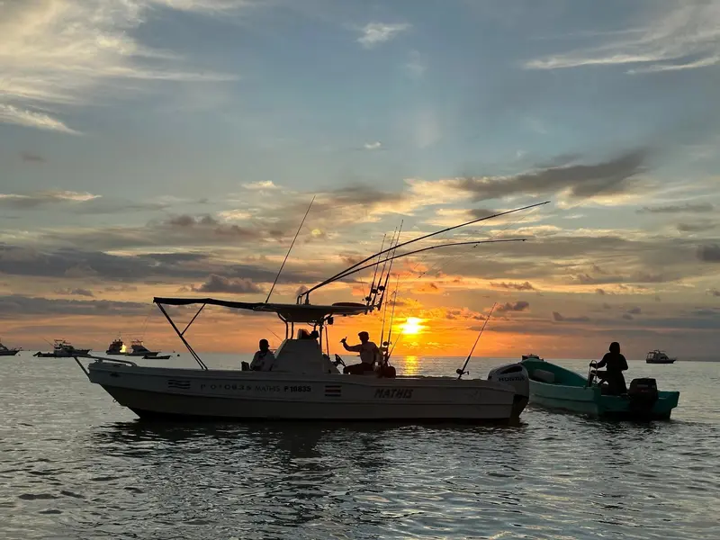 Lancha de pesca con cañas contra el atardecer anaranjado en el mar