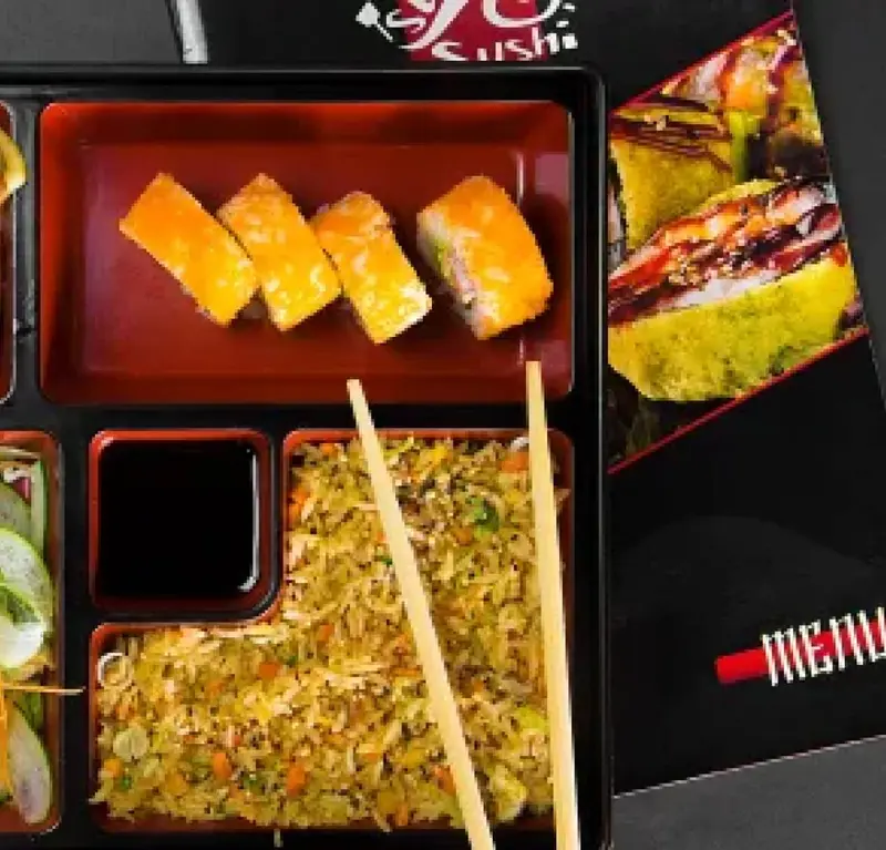 Caja bento con rollos de sushi, arroz frito y salsa de soya