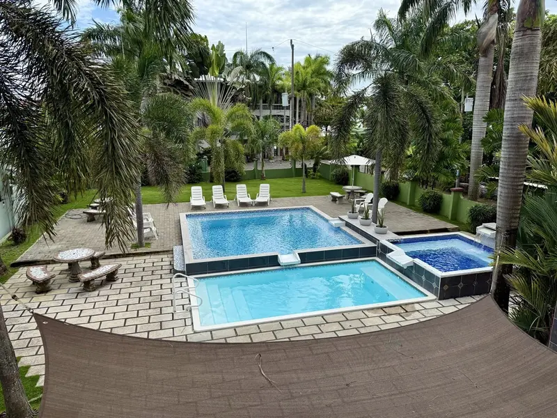 Vista desde arriba de dos piscinas y un jacuzzi en un patio de adoquines entre palmeras