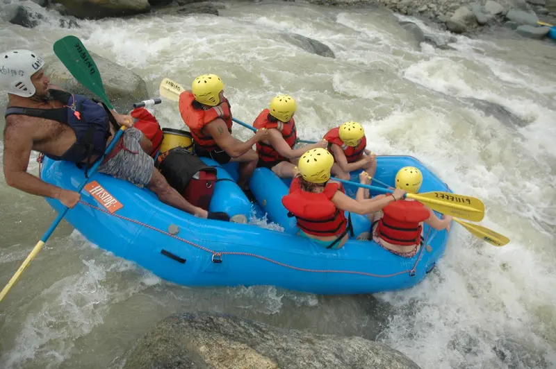 Balsa azul con rafters con casco y chaleco remando en rápidos blancos