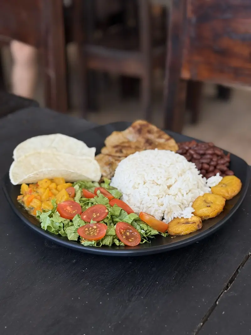 Plato típico en una mesa oscura con arroz, frijoles, ensalada, plátano maduro y tortilla