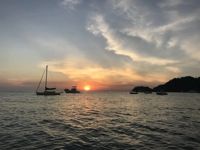Atardecer anaranjado sobre el mar con un velero anclado y una isla al fondo