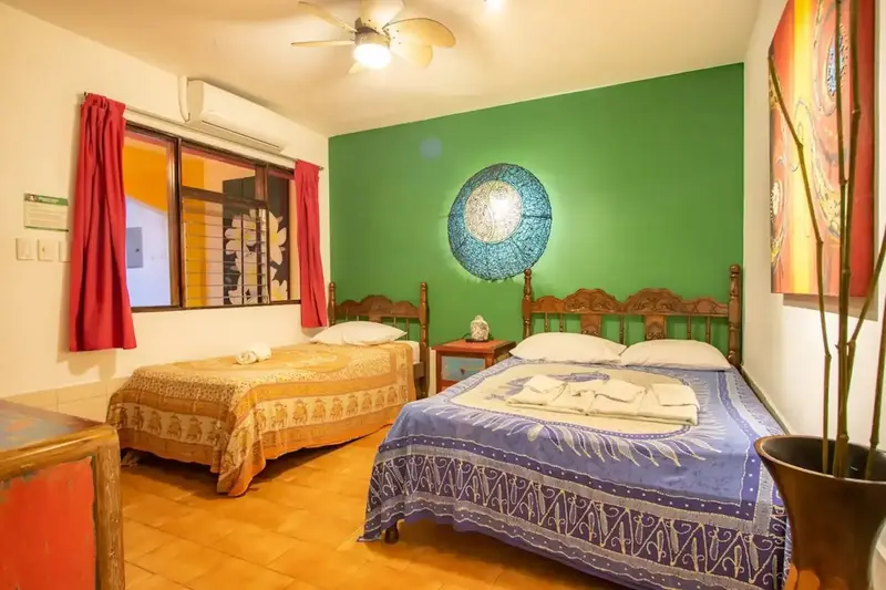 Habitación con pared verde, dos camas y cortinas rojas