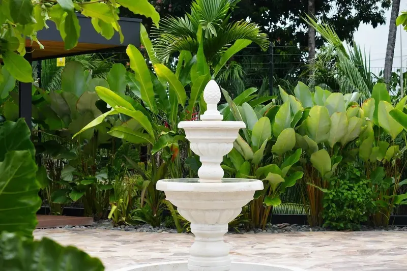 Fuente blanca de tres niveles rodeada de plantas tropicales en el jardín
