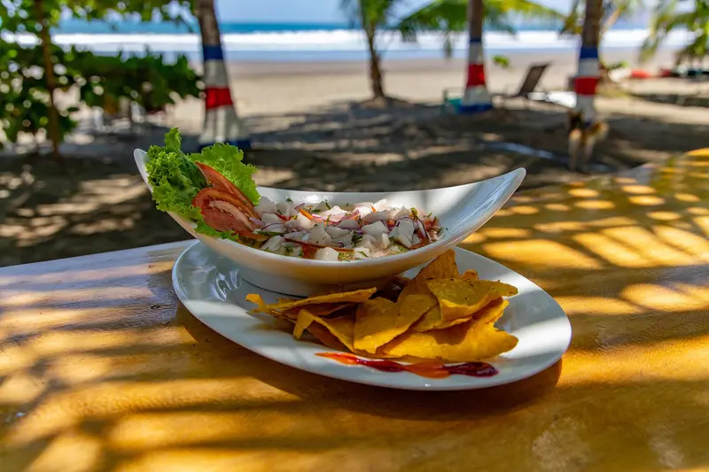 Ceviche en un tazón con chips de tortilla sobre una mesa, con la playa al fondo