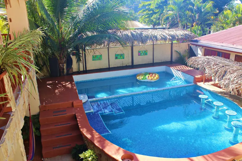 Piscina azul con deck de madera, palmeras y techo de palapa