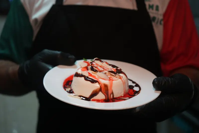 Panna cotta con salsa roja sobre un plato blanco que sostiene un camarero