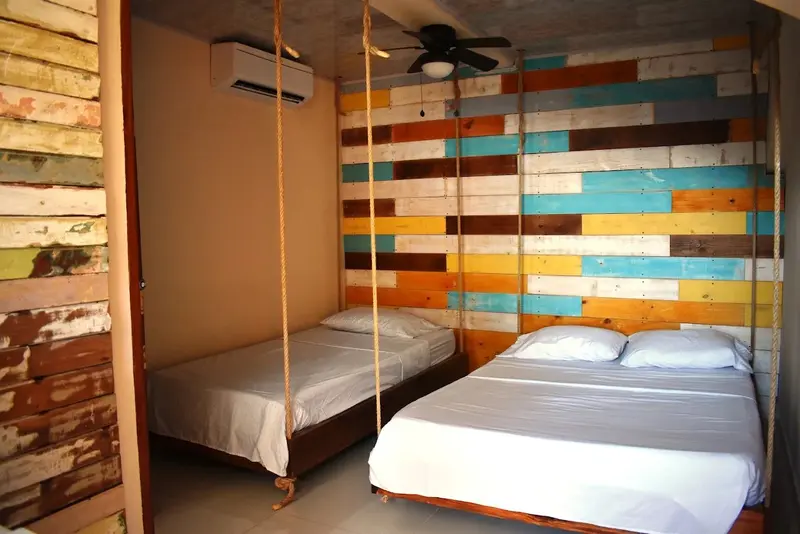 Habitación con dos camas suspendidas de cuerdas y una pared de tablones de colores