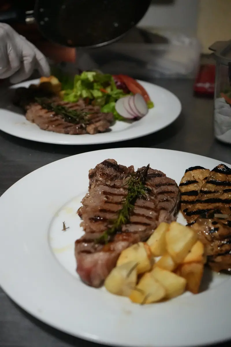 Plato con dos cortes de carne a la parrilla y papas, y una ensalada al fondo
