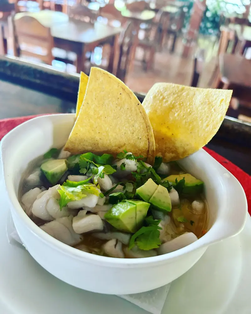 Ceviche en un bowl blanco con aguacate, cebolla y cilantro, servido con chips de tortilla