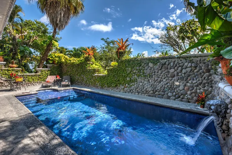 Piscina privada de agua azul rodeada de vegetación y muros de piedra
