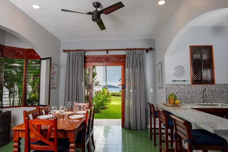 Comedor y cocina de un condominio de dos dormitorios, con vista al jardín y al mar por la puerta abierta